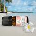 Bottle of Beach Vibes Essential Oil Blend on a beach with blurred ocean and palm trees in background and a tropical flower in front.